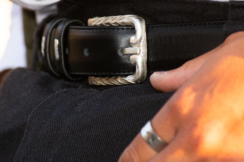 Empire line silver belt buckle on black leather with hand chased edges, worn with a wide silver ring and black trousers.