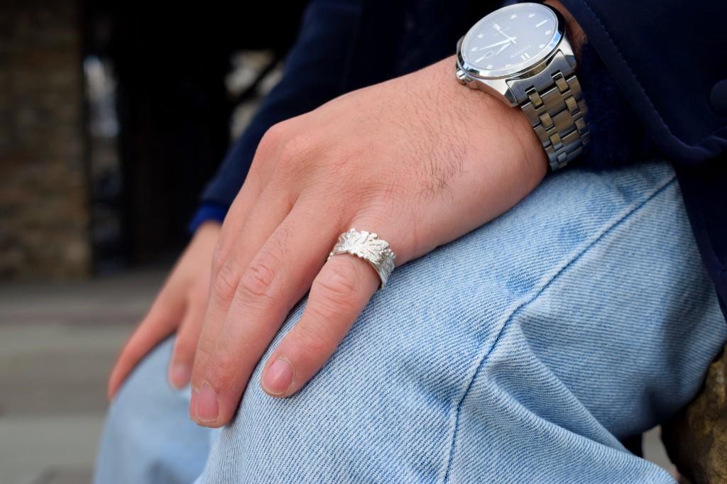 Hand worn wide silver ring with acanthus style hand chasing, with a watch and denim in natural light.