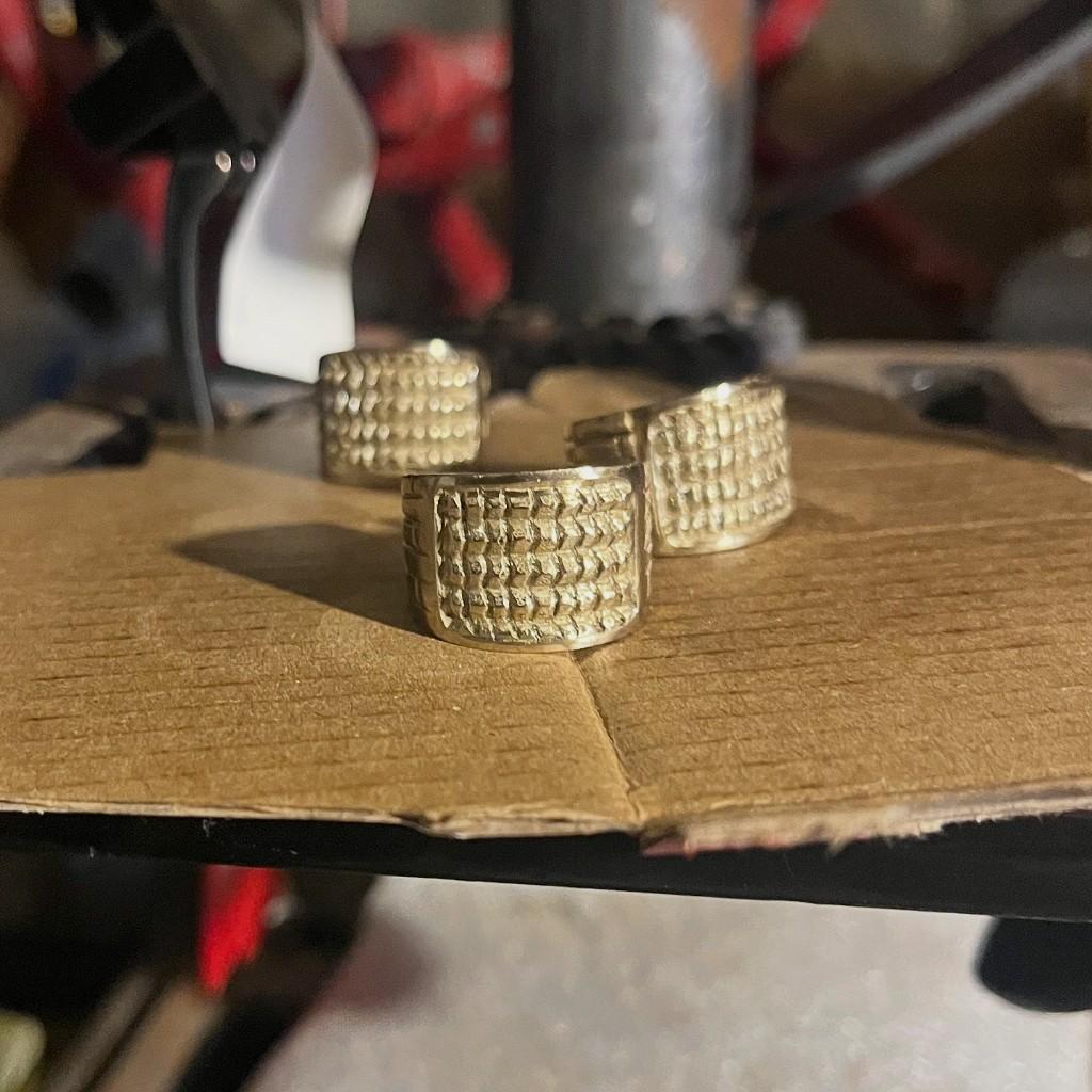Textured solid brass band rings in progress on a workshop surface.