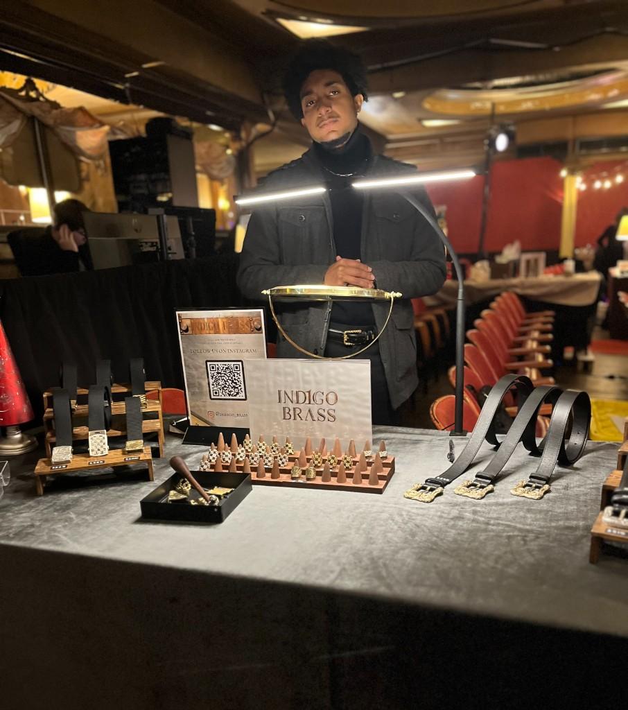 Indigo Brass at a show: display table, rings, belts, and lit studio sign.